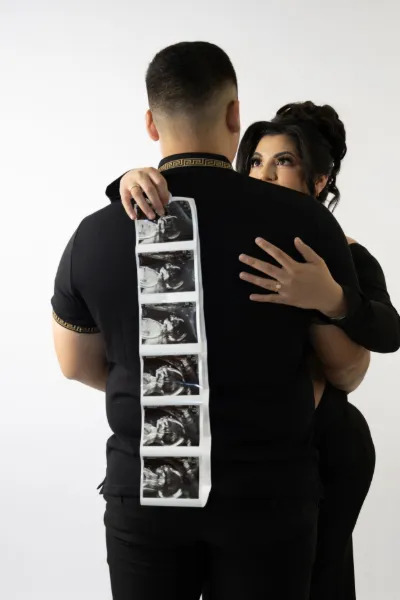 Couple embraces while displaying ultrasound photos on man's back announcing their pregnancy.