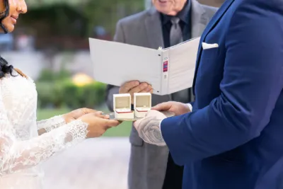 Close-up of wedding ring exchange ceremony with officiant holding book and couple in elegant attire.