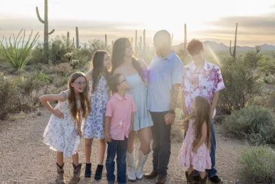 Large family group posing together in a sun-drenched desert landscape with towering saguaro cacti at dusk.