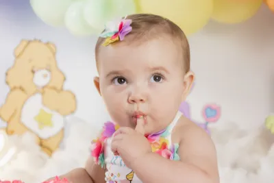 An adorable baby girl with a colorful bow headband at a Care Bears themed first birthday celebration.