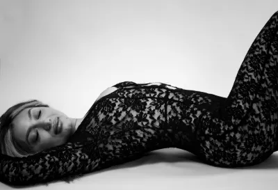 Black and white artistic photo of a woman lying down wearing a sheer black lace bodysuit.